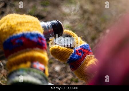 Hands in colorful mittens pouring a hot drink from thermos Stock Photo