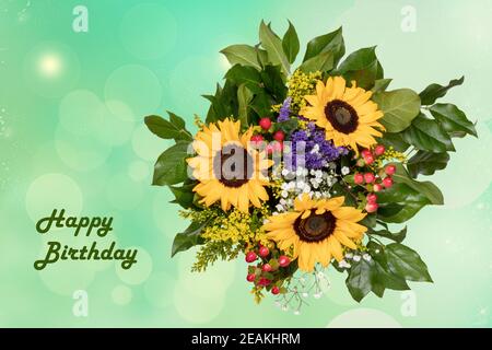 Happy birthday card design with a gorgeous blooming bouquet of sunflowers on a bright abstract delicate pastel green blurred background. Stock Photo