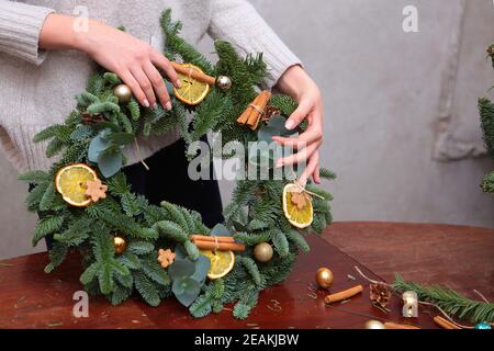 Christmas decoration is made by hand. The traditional Christmas wreath is decorated with oranges and cinnamon. Photos without a face. Stock Photo