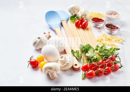 Food background with place for text, with different kinds of pasta, tomatoes, herbs, mushrooms, eggs, seasonings scattered on light marble background. Stock Photo