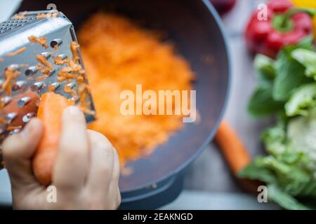 Female hands firmly grating a carrot into a bowl Stock Photo