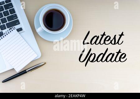 LATEST UPDATE text with fountain pen, notepad, laptop and cup of coffee on wooden background Stock Photo