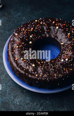 Christmas homebaked dark chocolate bundt cake on a blue plate decorated with chocolate icing and multicolored sugar sprinkles. Stock Photo