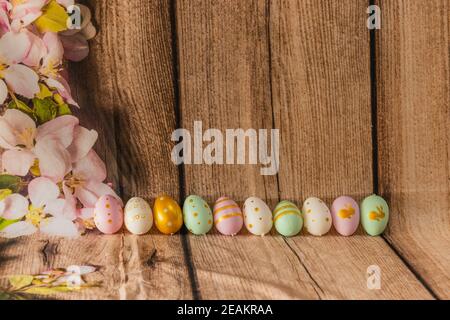 Closeup of colorful neatly arranged Easter eggs on a wooden surface with freshly picked flowers Stock Photo