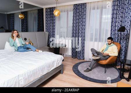 Interracial couple using smartphone and laptop in hotel room Stock Photo