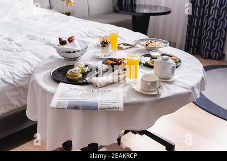 Newspaper near breakfast and drinks on table in hotel room Stock Photo