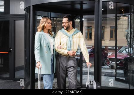 Cheerful arabian man with luggage looking at girlfriend near hotel entrance Stock Photo