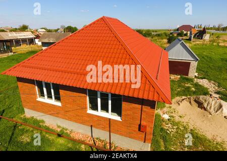 House with an orange roof made of metal, top view. Metallic profile painted corrugated on the roof. Stock Photo