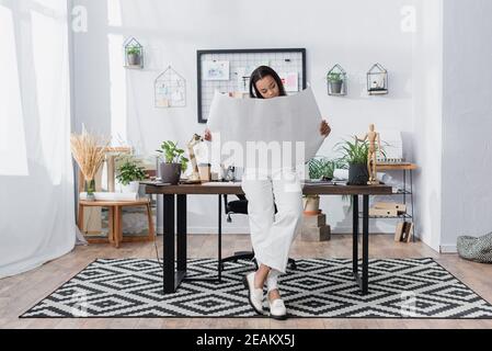 african american architect holding project while leaning on desk at home studio Stock Photo