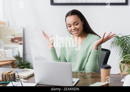 amazed african american architect gesturing at workplace near laptop and coffee to go Stock Photo