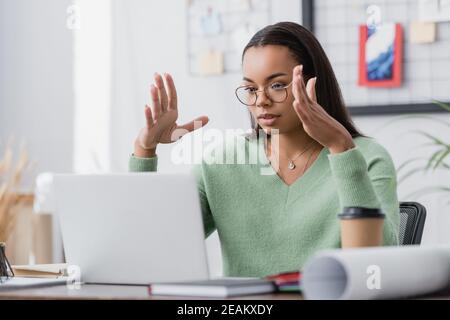 young african american interior designer gesturing while looking at laptop on blurred foreground Stock Photo