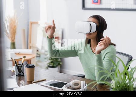african american freelance architect gesturing while using vr headset at workplace, blurred foreground Stock Photo