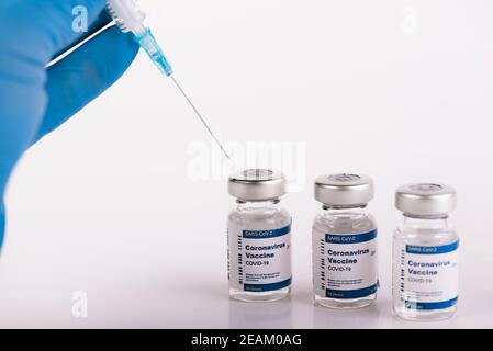 Hands with blue latex gloves syringe taking anti covid vaccine from vial Stock Photo