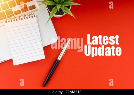 LATEST UPDATE text with notepad, laptop, fountain pen and decorative plant on red background. Stock Photo