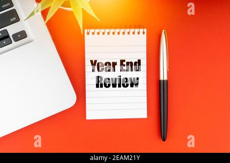 YEAR END REVIEW text with notepad, laptop, fountain pen and decorative plant on red background. Stock Photo