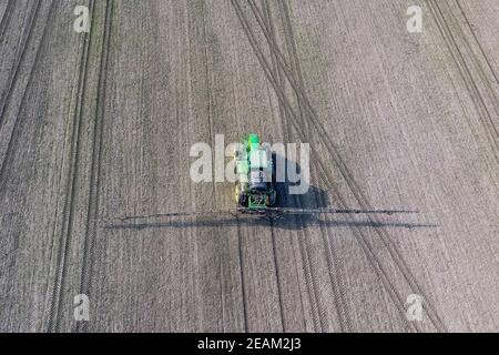 Tractor with hinged system of spraying pesticides. Fertilizing with a tractor, in the form of an aerosol, on the field of winter wheat. Stock Photo