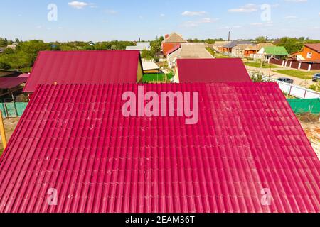 A house with a red roof made of corrugated metal sheets. Roof from corrugated metal profile. Metal tiles. Stock Photo