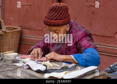 Xizhou, China - April 26, 2019: Portrait of an elderly woman at work at Xizhou old market. She's working on soles for the typical bai people shoes Stock Photo