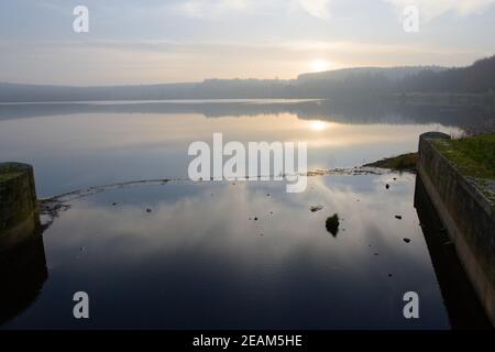 Redmires reservoir dam inlet overflow reflecting a misty water sunset Stock Photo
