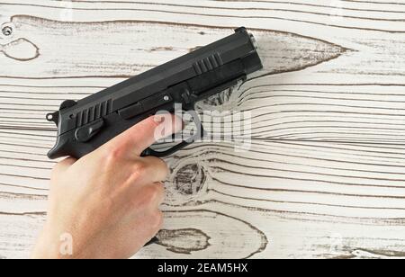 Man hand holding black modern metal gun on white wooden table, closeup detail Stock Photo