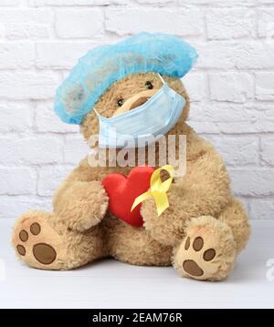 brown teddy bear holds in his paw a yellow ribbon folded in a loop Stock Photo