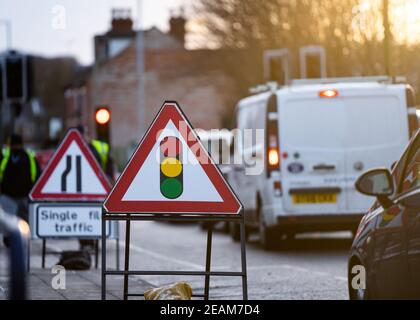 Temporary traffic lights triangle warning sign and traffic light showing red stop signal in background with queuing traffic jam at roadworks on sunny Stock Photo