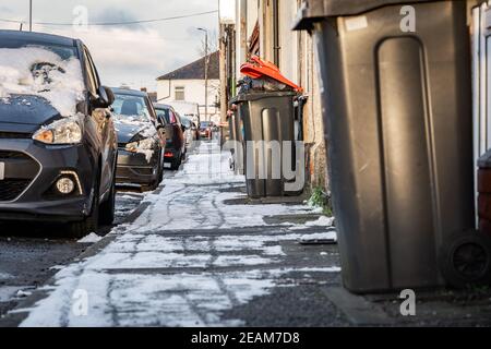Dustbins overflowing left out on the street and pavement in town uncollected by council with lids open no wheelie bin recycling refuse collection snow Stock Photo
