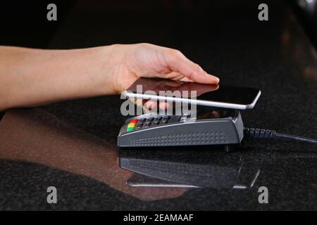 Payment by cell phone. Payment by cell phone through the terminal in the restaurant, shop. Women's hand close-up with cell phone when paying for the purchase. Stock Photo