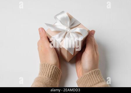 Beige gift box with white bow in woman hands on white background Stock Photo