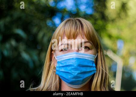 Middle aged woman wearing blue virus mouth nose mask nice backlight sun bokeh in background closeup face portrait People with facemask Concept copy Stock Photo