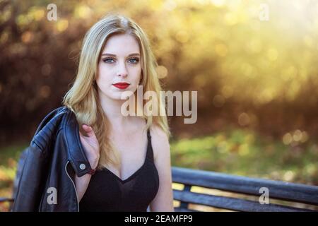Attractive girl is sitting on a bench in autumn park. Horizontally. Stock Photo