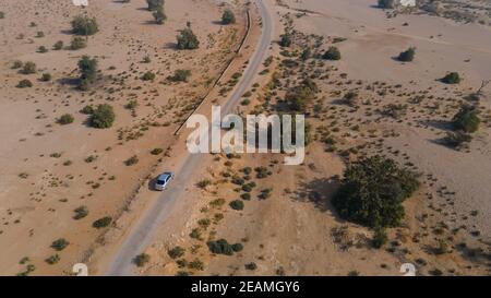 Aerial view of silver car driving on country road in desert. Shot from drone flying over road. Stock Photo