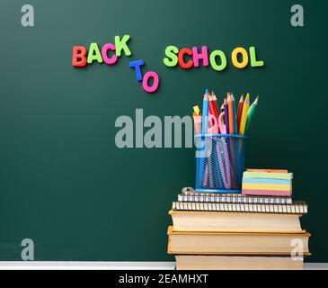 stack of books and stationery on empty chalk green chalkboard background Stock Photo