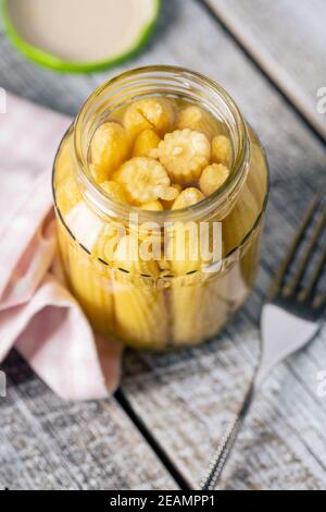 Pickled young baby corn cobs in jar. Stock Photo