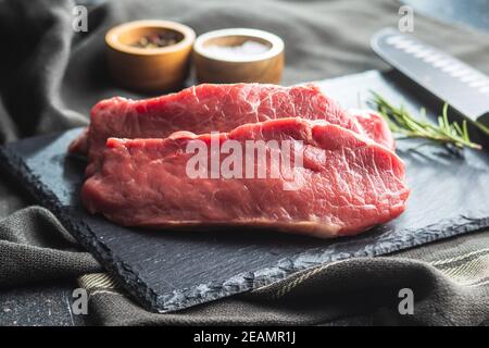 Slices raw striploin steak on black stone cutting board. Stock Photo