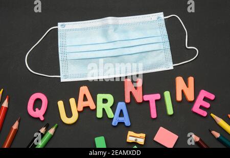 inscription quarantine from multicolored plastic letters and school supplies on black chalk board Stock Photo