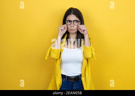 Young brunette businesswoman wearing yellow blazer over yellow background depressed and worry for distress, crying angry and afraid. Sad expression. Stock Photo