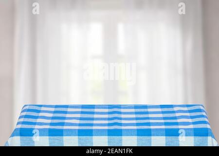 Empty table product. Closeup of a empty blue checkered tablecloth or napkin on a rustic bright table against blurred curtains background. Template for food and product display montage. Stock Photo