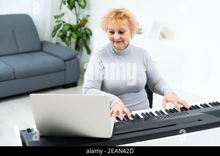 The woman plays the synthesizer and looks at the laptop screen. Close-up of female hands on the electric piano. Stock Photo