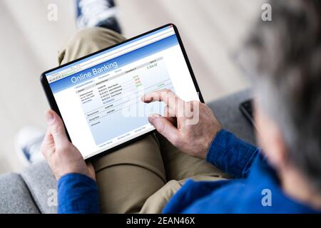 Man Using Tablet Computer Checking Bank Statement Stock Photo
