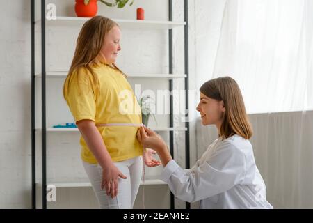 Friendly nutritionist measures girl's waist. Childhood obesity Stock Photo