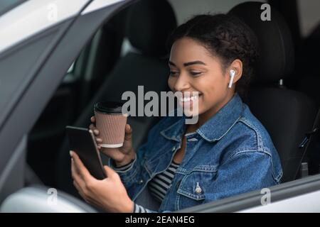 Portrait of young and cheerful woman with coffee cup sits in car in city on break Stock Photo