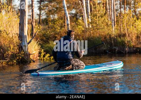 Young athletic man on a stand-up paddleboard at sunset in the lake - the summer evening activity Stock Photo