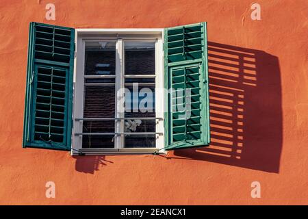 window with open shutter and flower in an old house in the countryside, shadow on the wall Stock Photo
