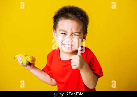 kid cute little boy attractive smile playing holds bananas and show finger thumb for good sign Stock Photo