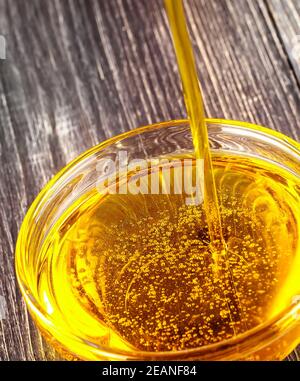 Pouring cooking oil a small glass cup on old wooden table Stock Photo