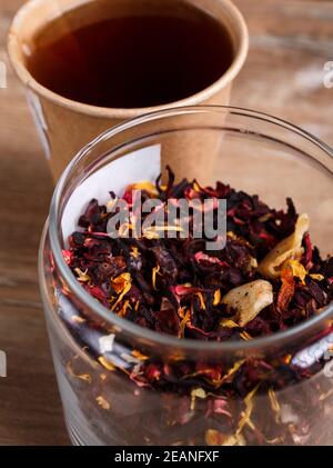 Glass with leaf of karkade tea and brewed tea in disposable paper cup on wooden rustic background. Stock Photo