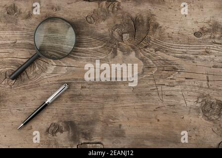 Magnifying glass and a pen lying on old wooden texture Stock Photo