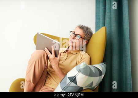 Mature woman sitting on armchair at home  Stock Photo