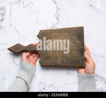 two female hands hold an empty old brown rectangular wooden cutting board Stock Photo